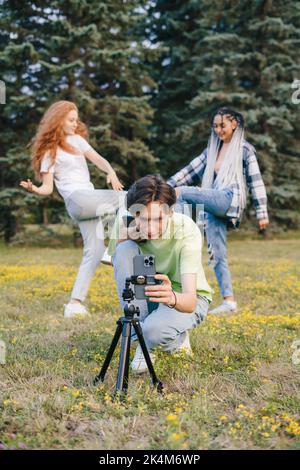 Gruppe kaukasischer Freunde, die Videoblog für soziale Netzwerke drehen und das Mobiltelefon auf einem Stativ verwenden, um im Sommerpark zu senden. Video für soziale Medien Stockfoto