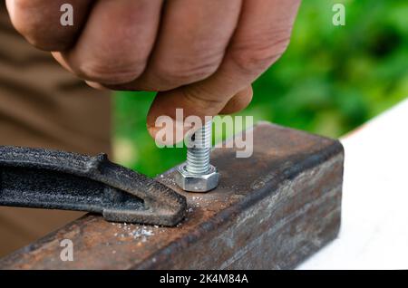 Eine Männerhand schraubt einen Bolzen in eine Metallmutter. Arbeiten mit Metall Stockfoto