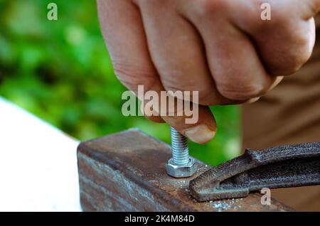 Eine Männerhand schraubt einen Bolzen in eine Metallmutter. Arbeiten mit Metall Stockfoto