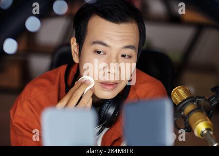 Selektiver Fokus, mittlere Nahaufnahme eines modernen jungen asiatischen männlichen Influencers, der neue Gesichtspulver für Werbung oder Beauty-Produktbewertung anwendet Stockfoto