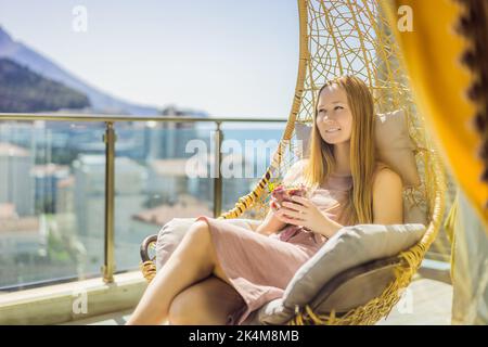 Portrait einer wunderschönen Frau in einem wunderschönen Kleid, die auf einer Terrasse sitzt und Erdbeere isst Stockfoto