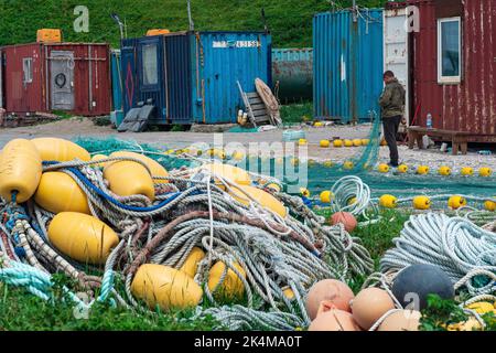 Lagunnoe, Russland - 01. August 2022: Fischer überprüft und repariert industrielle Fischernetze am Ufer eines Fischereistützpunkes Stockfoto