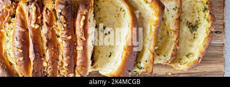 Hausgemachtes frisches Pull-Apart-Brot mit Kräutern (Petersilie, Thymian, Rosmarin, Dill), Knoblauch, Käse und würzige Butter auf einem Holzbrett, Banner. Stockfoto