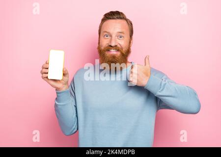 Portrait von positiven fröhlich roten Haar Kerl blau lange Ärmel Demonstration Smartphone zeigt Daumen nach oben isoliert auf rosa Hintergrund Stockfoto