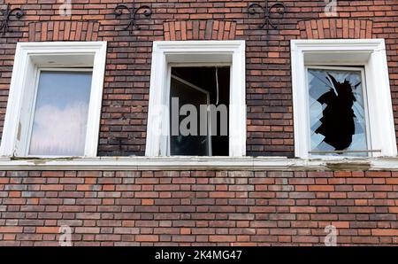 Symbolisches Bild: Verlassen. Leer, Vergangenheit, kaputt: Hausfassade aus Ziegensteinen mit einem ganzen Fenster, leerem und gebrochenem Fenster Stockfoto