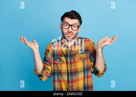 Foto von schönen jungen verwirrt Kerl in Brillen gekleidet karierten Hemd Frage zuckende Schultern isoliert auf blauem Hintergrund Stockfoto