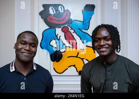 London, Großbritannien. 3. Oktober 2022. Die Mitbegründer der EFIE Gallery (L) Kobi und Kwame Mintah mit „Jonny Just Come“, 2022, von Slawn. Vorschau auf 'On A Darker Note', eine Ausstellung mit Werken des nigrischen Londoner Künstlers Slawn in der Arabischen Britischen Handelskammer in Mayfair. Die neuen Arbeiten konzentrieren sich auf Clowns, die auf die Karikaturen der Schwarzgesicht-Minstrel reagieren, die während der Ära der Jim Crow-Gesetze zur Rassentrennung in den USA im späten 19.. Und frühen 20.. Jahrhundert entstanden sind. Kredit: Stephen Chung / Alamy Live Nachrichten Stockfoto