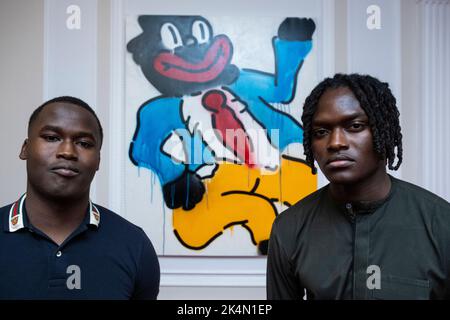 London, Großbritannien. 3. Oktober 2022. Die Mitbegründer der EFIE Gallery (L) Kobi und Kwame Mintah mit „Jonny Just Come“, 2022, von Slawn. Vorschau auf 'On A Darker Note', eine Ausstellung mit Werken des nigrischen Londoner Künstlers Slawn in der Arabischen Britischen Handelskammer in Mayfair. Die neuen Arbeiten konzentrieren sich auf Clowns, die auf die Karikaturen der Schwarzgesicht-Minstrel reagieren, die während der Ära der Jim Crow-Gesetze zur Rassentrennung in den USA im späten 19.. Und frühen 20.. Jahrhundert entstanden sind. Kredit: Stephen Chung / Alamy Live Nachrichten Stockfoto