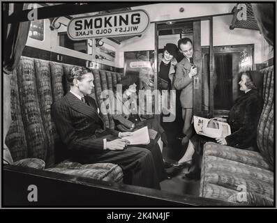 UK British Rail Vintage First Class Rail-Abteil mit „RAUCHEN“-Schild, gesponsert von Wills Gold Flake, und glückliche gut gekleidete Passagiere in einem komfortablen Eisenbahnwaggon, Tabakabteil, Archive Retro Britain UK 1936. Stockfoto