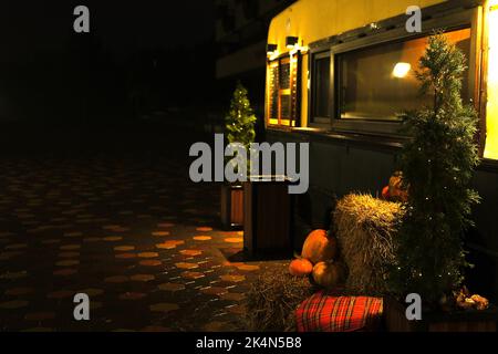 Halloween Hintergrund mit Textur orange Kürbisse auf dunklen strow Stapel in der Nähe Kaffee Anhänger Stand. Nahaufnahme von natürlichen rötlichen Kürbissen mit Wassertropfen fo Stockfoto