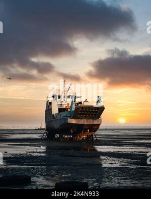 Eine vertikale Aufnahme eines alten Schiffes am Ufer bei einem schönen, weichen Sonnenuntergang Stockfoto