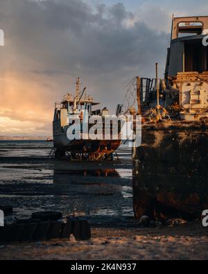 Eine vertikale Aufnahme eines alten Schiffes am Ufer bei einem schönen, weichen Sonnenuntergang Stockfoto