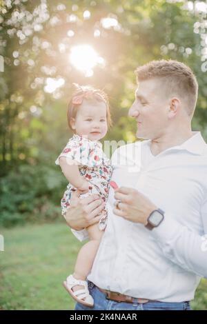 Der kaukasische Vater hält an sonnigen Tagen eine 1-jährige Tochter. Stockfoto