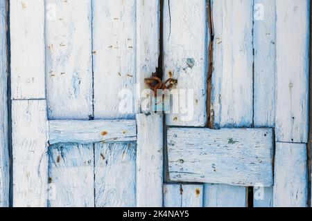 Geschlossene Holztür mit rostigen Vorhängeschloss-Hintergrund, Textur. Hellblaue leere, gealterte Eingangsplatten. Traditionelles griechisches Inselbauwerk. Stockfoto