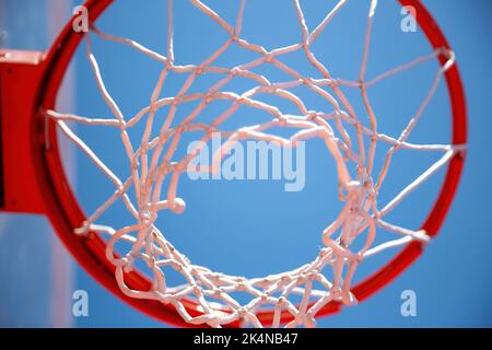 Basketballkorb, roter Ring und Netz, blauer Himmel im Hintergrund, Untersicht. Sonniger Tag, Sportplatz im Freien Stockfoto