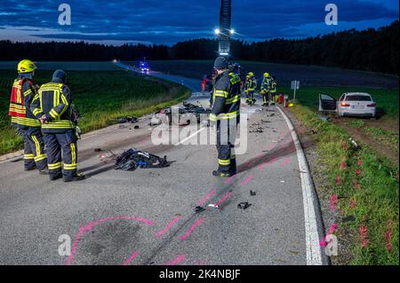 03. Oktober 2022, Bayern, Geiselhöring: Feuerwehrleute stehen neben einem zerstörten Motorrad und einem beschädigten Auto. Bei einem Unfall zwischen einem Auto und einer Gruppe von Motorradfahrern starb einer der Motorradfahrer. Ein zweiter Motorradfahrer wurde schwer verletzt ins Krankenhaus gebracht. Foto: Armin Weigel/dpa - ACHTUNG: Kennzeichen(e) wurden aus rechtlichen Gründen verpixelt Stockfoto