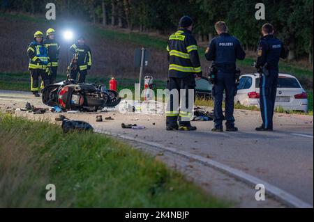 03. Oktober 2022, Bayern, Geiselhöring: Rettungskräfte stehen vor einem komplett zerstörten Motorrad neben einem Auto. Bei einem Unfall zwischen einem Auto und einer Gruppe von Motorradfahrern starb einer der Motorradfahrer. Ein zweiter Motorradfahrer wurde schwer verletzt ins Krankenhaus gebracht. Foto: Armin Weigel/dpa - ACHTUNG: Kennzeichen(e) wurden aus rechtlichen Gründen verpixelt Stockfoto