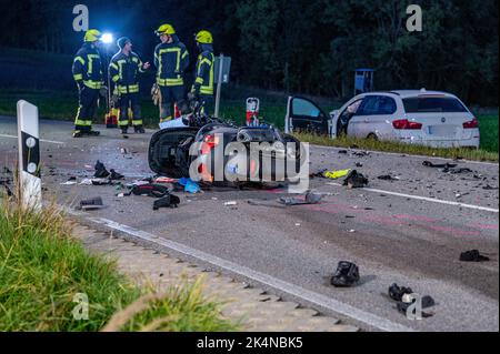 03. Oktober 2022, Bayern, Geiselhöring: Feuerwehrleute stehen hinter einem komplett zerstörten Motorrad und einem beschädigten Auto. Bei einem Unfall zwischen einem Auto und einer Gruppe von Motorradfahrern starb einer der Motorradfahrer. Ein zweiter Motorradfahrer wurde schwer verletzt ins Krankenhaus gebracht. Foto: Armin Weigel/dpa - ACHTUNG: Kennzeichen(e) wurden aus rechtlichen Gründen verpixelt Stockfoto