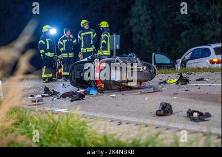 03. Oktober 2022, Bayern, Geiselhöring: Feuerwehrleute stehen hinter einem komplett zerstörten Motorrad und einem beschädigten Auto. Bei einem Unfall zwischen einem Auto und einer Gruppe von Motorradfahrern starb einer der Motorradfahrer. Ein zweiter Motorradfahrer wurde schwer verletzt ins Krankenhaus gebracht. Foto: Armin Weigel/dpa - ACHTUNG: Kennzeichen(e) wurden aus rechtlichen Gründen verpixelt Stockfoto