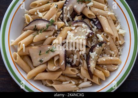 Penne-Pasta mit Steinpilzen, Parmesankäse, Rosmarin und Knoblauch auf dem Teller. Draufsicht auf Holztisch Stockfoto