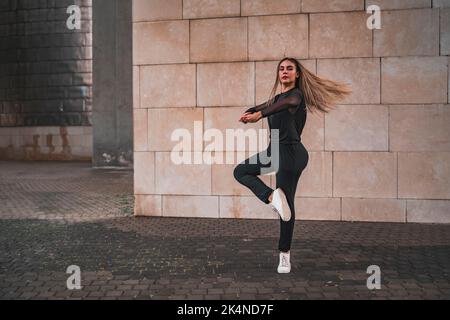 Eine junge Ballerina in schwarzem Anzug spielt auf der Straße Pirouetten zum Ballett. Stockfoto