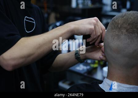 Der professionelle Meisterbarbier rasiert den Bart des Kunden mit einem elektrischen Trimmer. Haarschnitt des Bartes eines Mannes in einem Friseurladen. Barbier Men. Werbung und b Stockfoto
