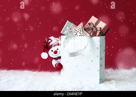 Weihnachts-Schneemann mit Einkaufstasche auf Schnee und Weihnachtsgeschenk. Banner für Winterangebote. Liefergeschenke. Schneemann verschenken Stockfoto