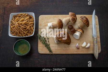 Draufsicht auf die Zutaten für Pasta-Pilze Gericht. Frische Steinpilze, Nudeln, Knoblauch, Rosmarin und Olivenöl auf dem Tisch Stockfoto