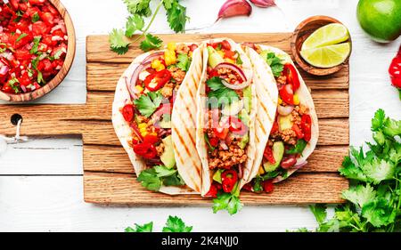 Mexikanische Küche. Tacos mit Rindfleisch, Mais, roten Bohnen, Tomatensalsa-Sauce und Zwiebeln in Maistortilla an Bord. Weißer Tischhintergrund, Draufsicht Stockfoto