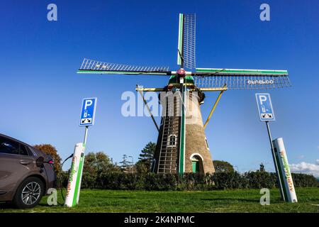 Strom aus Windenergie: Parkplatz mit Ladestation für Elektrofahrzeuge vor der historischen Windmühle aus dem Jahr 1817 in Domburg, Niederlande Stockfoto
