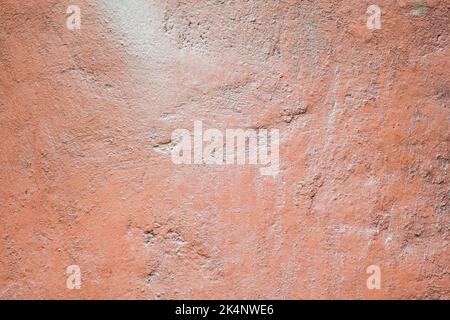 Die Textur des alten lackierten Betons. Der Betonhintergrund ist staubrosa. Der Hintergrund einer bemalten Wand mit Rissen. Stockfoto