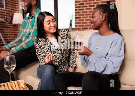 Kulturelle unterschiedliche Nationalitäten, Ethnien Frauen plaudern, reden, diskutieren fröhlich während des Treffens von Hausfreunden, trinken Wein, essen Brotstäbchen, Käse. Stockfoto
