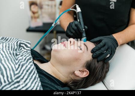 Ein Gesundheitsdienstleister, der einem Patienten eine nicht-invasive Gesichtsbehandlung zur Reinigung, Extraktion, Peeling und Hydratation gibt Stockfoto