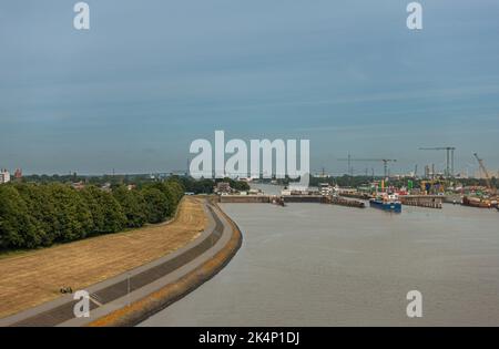 Brunsbuttel, Deutschland - 12. Juli 2022: Weite Landschaft unter teilweise wolkig-blauem Himmel der Kieler Kanal Schleusen mit eindringendem Schiff. Graues Nordsee-Wasser U Stockfoto