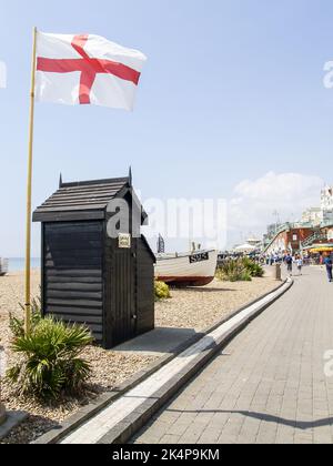 Brighton Beach Vereinigtes Königreich - Juni 16 2009; kleines dunkelbraunes Gebäude mit Rauchhaus am Türschild und Flagge von England neben dem Weg entlang des Be Stockfoto