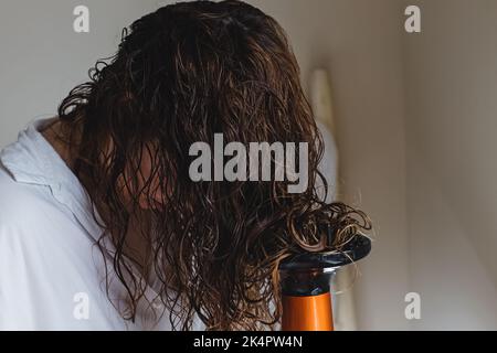 Frau diffundiert ihre Haare mit einem Trockner. Trocknen des Haares nach einer lockigen Methode für das Haarstyling Stockfoto