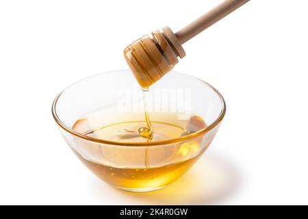 Honig- und Honigtauchen in Glasschale auf weißem Hintergrund. Honig tropft aus dem Honigtauer. Stockfoto