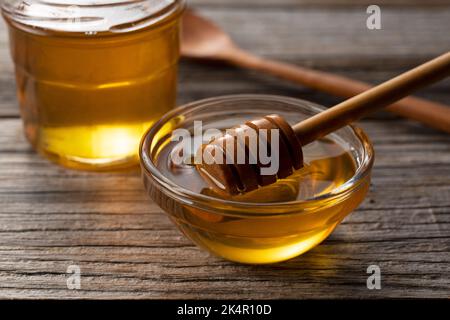 Honig und Honig aus Holz in Glasbehälter auf altem Holzhintergrund. Honig tropft aus dem Honigtauchmittel. Stockfoto