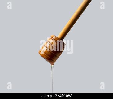 Honig und Holzhonig Dipper auf grauem Hintergrund. Honig tropft aus dem Honigtauchmittel. Nahaufnahme. Stockfoto