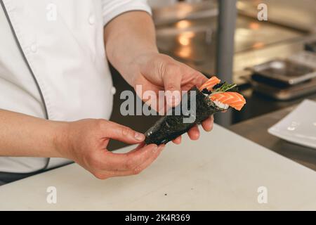 Der Koch kocht Sushi mit Reis, Lachs und Nori in der Küche des japanischen Restaurants Stockfoto