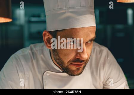 Nahaufnahme eines fokussierten männlichen Küchenchefs in Uniform, der in der Küche des Restaurants steht und wegschaut Stockfoto