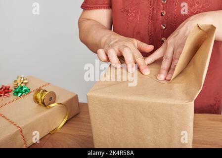 Unkenntlich reife Frau, die Weihnachtsgeschenke zu Hause verpackt. Sauberes Design mit Platz für Kopien. Stockfoto