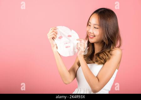 Gesundheitszentrum. Asiatische Frau hält reinigende Maske Gesicht auf den Händen, Portrait schön weiblich lächelnd hält Gesichtsmaske, Studio Schuss isoliert auf b Stockfoto