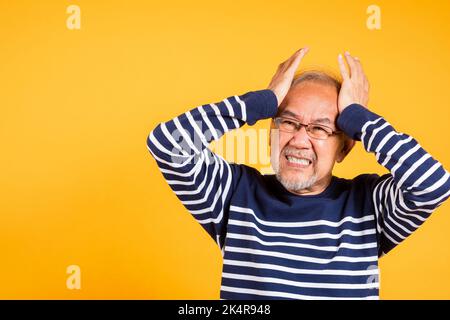 Porträt älterer alter Mann traurig an Migräne leiden Studio geschossen isoliert auf gelbem Hintergrund, asiatische ältere Mann Hände halten Kopf und nahe Ohren ersticken Stockfoto