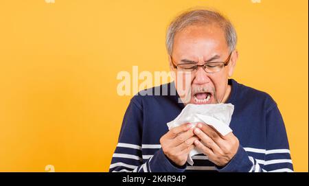 Asiatische ältere Mann Erkältung mit Grippe und Niesen von Krankheit Virus Problem verwenden Gewebe Studio Schuss isoliert auf gelbem Hintergrund, Portrait älterer alter Mann Stockfoto