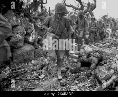 OKINAWA, PAZIFISCHER OZEAN - 1945. April - US-Marineinfanteristen passieren ein kleines Dorf, in dem japanische Soldaten nach dem Kampf gegen japanische Truppen auf Okina tot lagen Stockfoto