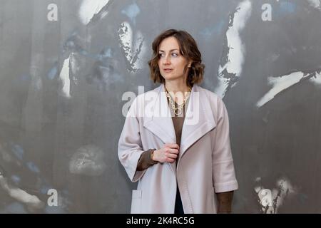 Modische und stilvolle Mädchen posiert in grünen Culottes, einem Pullover und einem leichten Mantel an einer grauen Wand Stockfoto