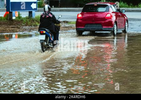 Frau fahren Motorrad durch überflutete Straße. Motorradfahren auf überfluteter Straße während der Überschwemmung durch sintflutartige Regenfälle. Überflutete Straße mit großen Stockfoto