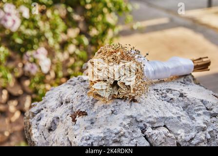 Bouquet von getrockneten Rosen gebunden mit weißem Band auf Felsen bei Sonnenuntergang liegen Stockfoto
