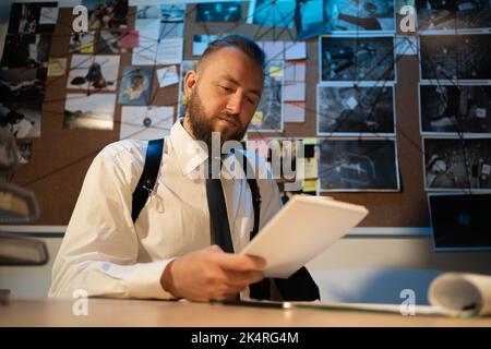 Detective, der am Schreibtisch in seinem Büro am Arbeitsplatz mit Dokumenten arbeitet, während er während der Ermittlungen kriminelle Profile lernt. Detektivverarbeitung Stockfoto